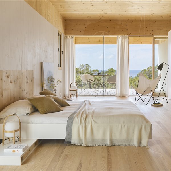Dormitorio de una casa en madera natural con sabanas de lino y ventana