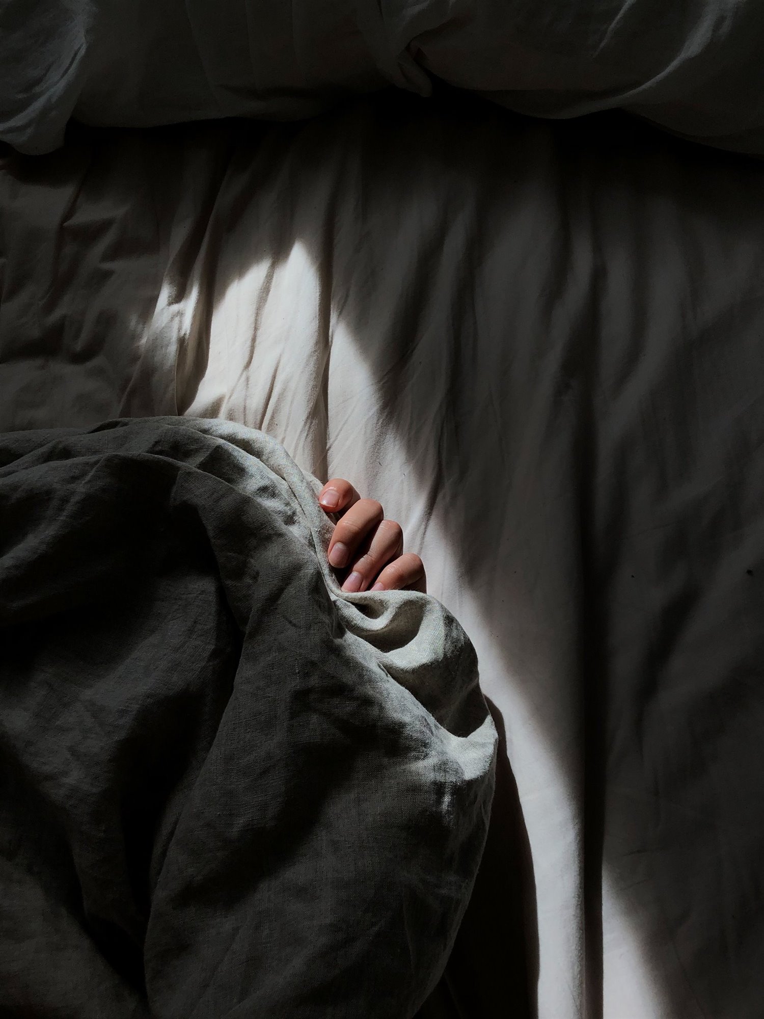 mujer durmiendo en un colchon con sabanas de color gris