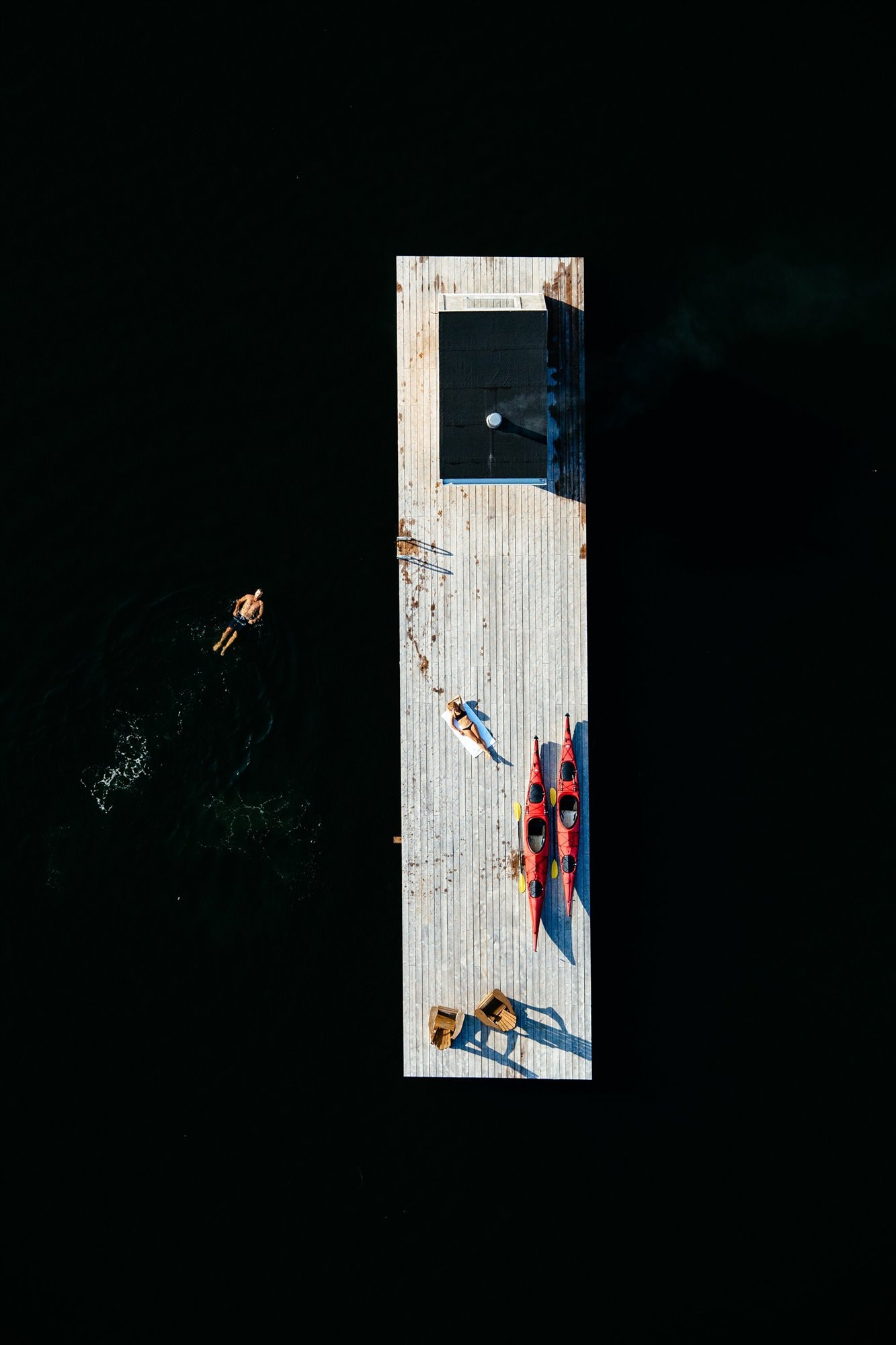 Cabaña moderna con Sauna de madera flotando en mitad de un lago vista aerea con hombre nadando
