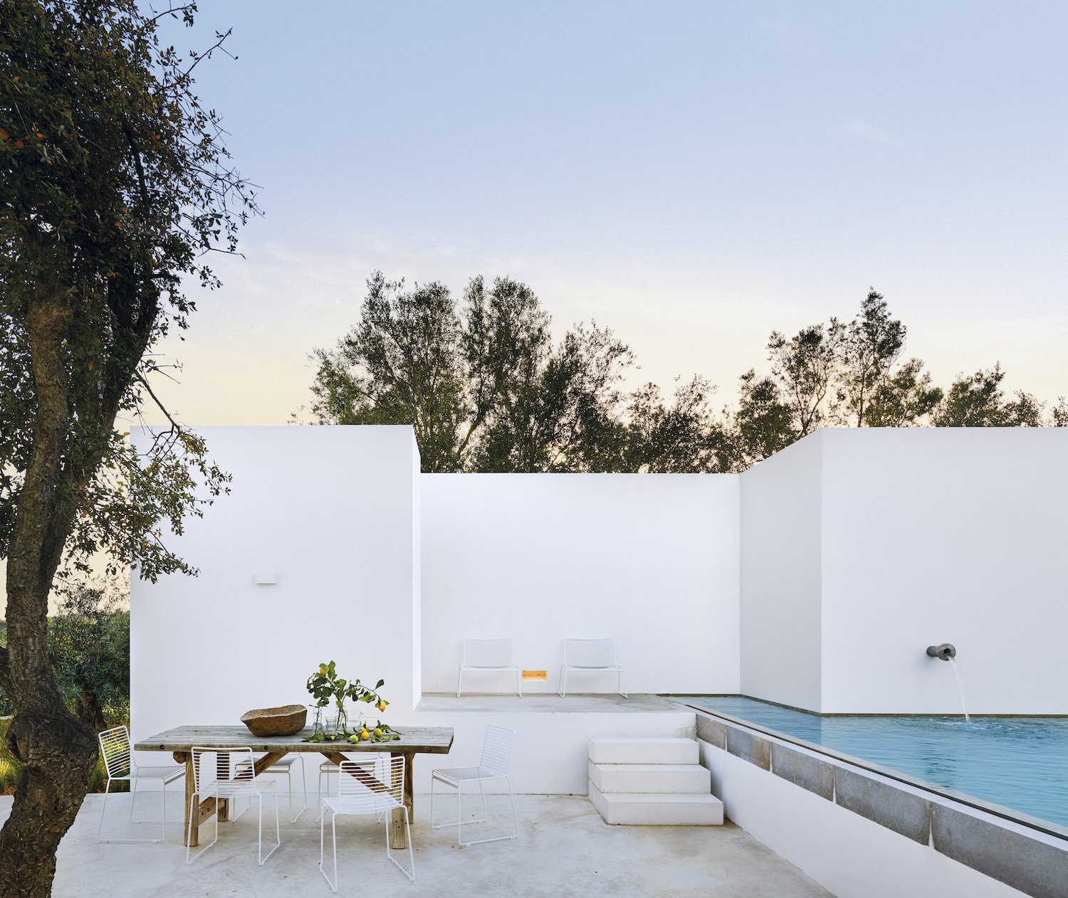 Comedor exterior con mesa de madera y sillas blancas de una casa con piscina