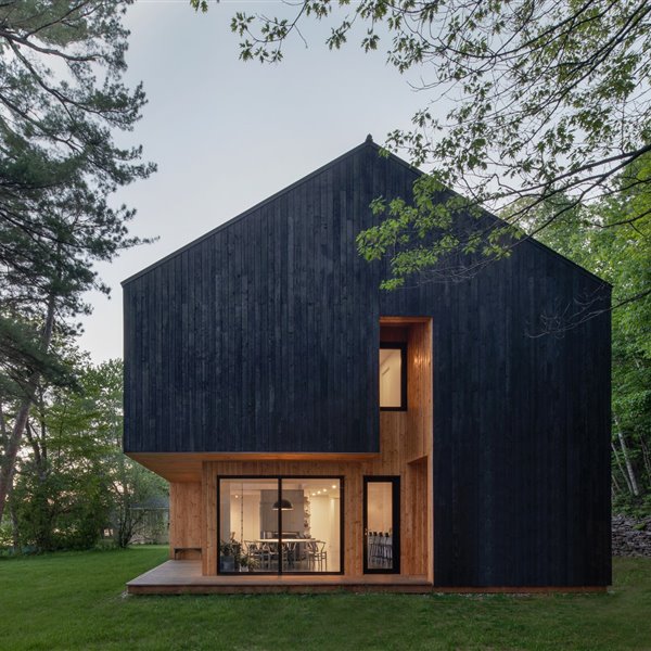 Una moderna cabaña de madera negra proyectada junto a un lago