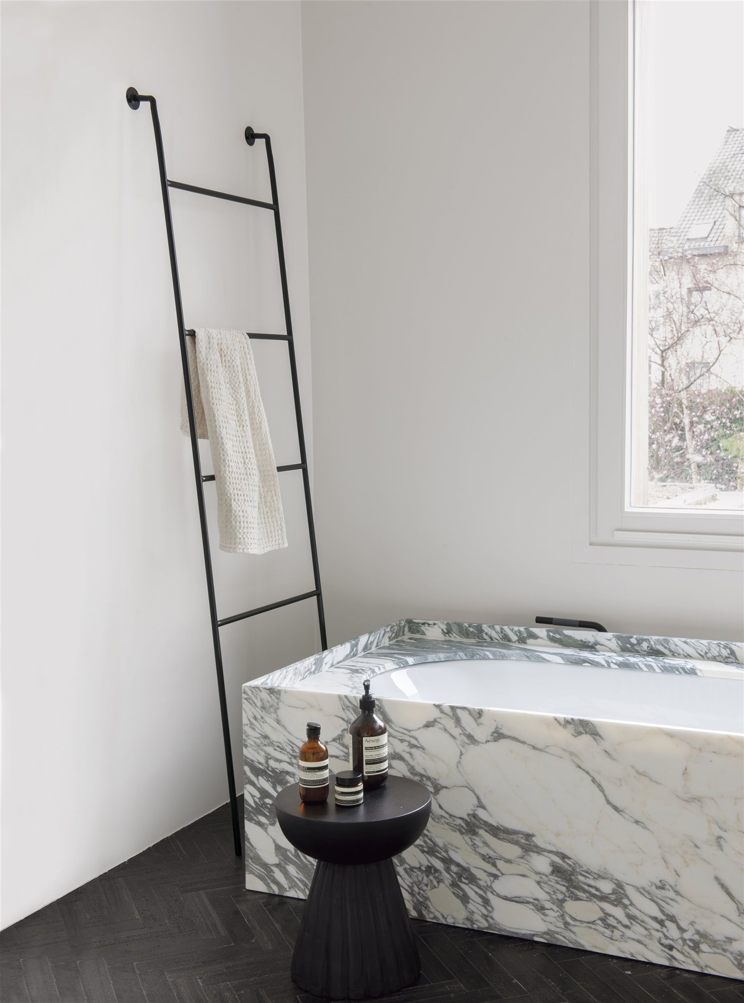Baño con bañera de marmol y escalera negra con una toalla blanca. Lavadora