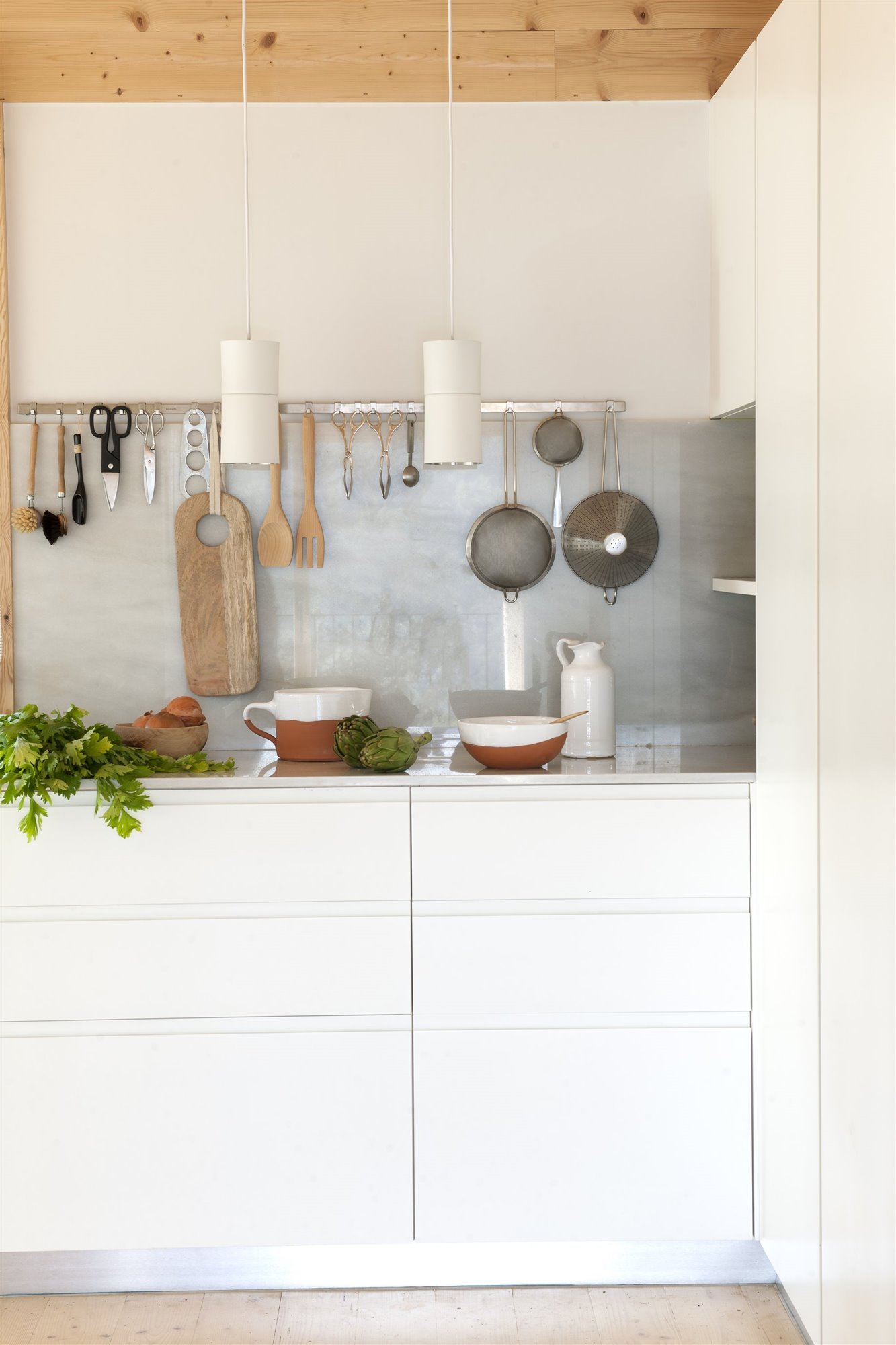 Cocina con muebles en color blanco y barra para colgar los utensilios foto Pere Peris