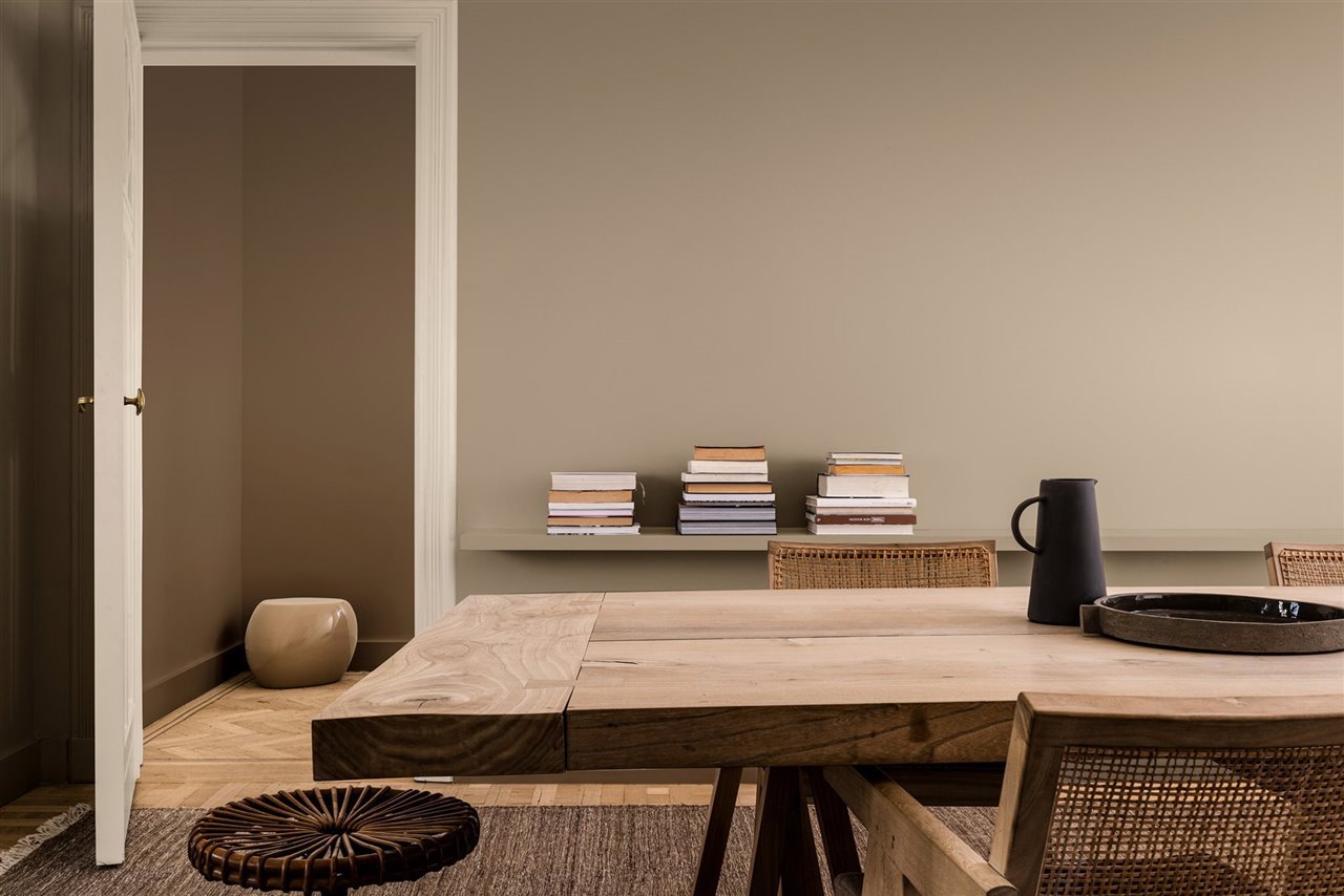 Salon con mesa de madera y libros paredes en color beige. Reproducir con fidelidad
