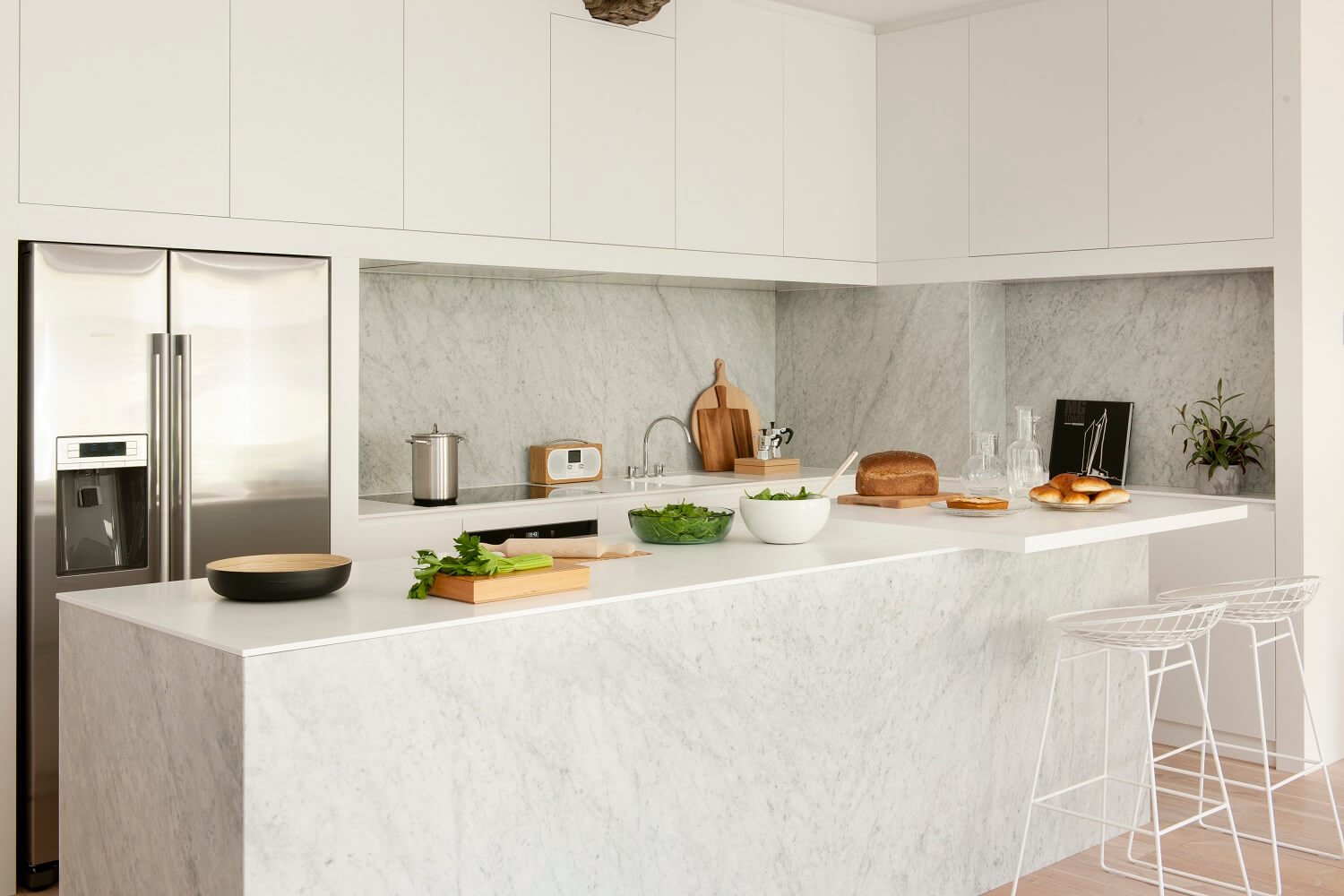 Cocina blanca de mármol con isla y sillas altas