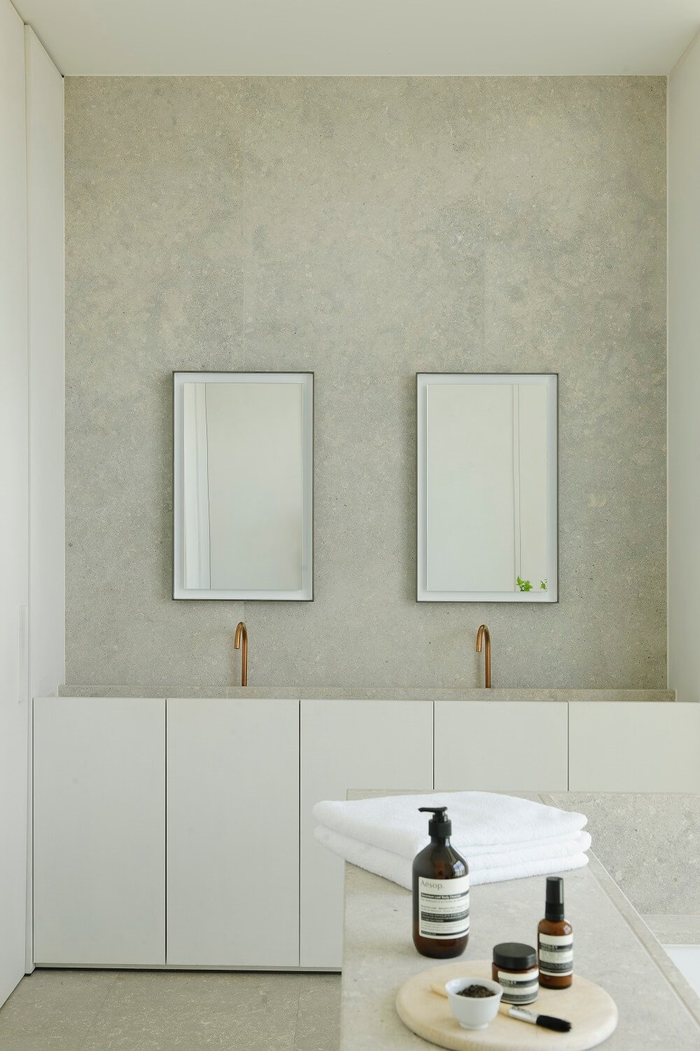 Mueble de baño blanco con grifería encastrada dorada dos espejos y pared gris.