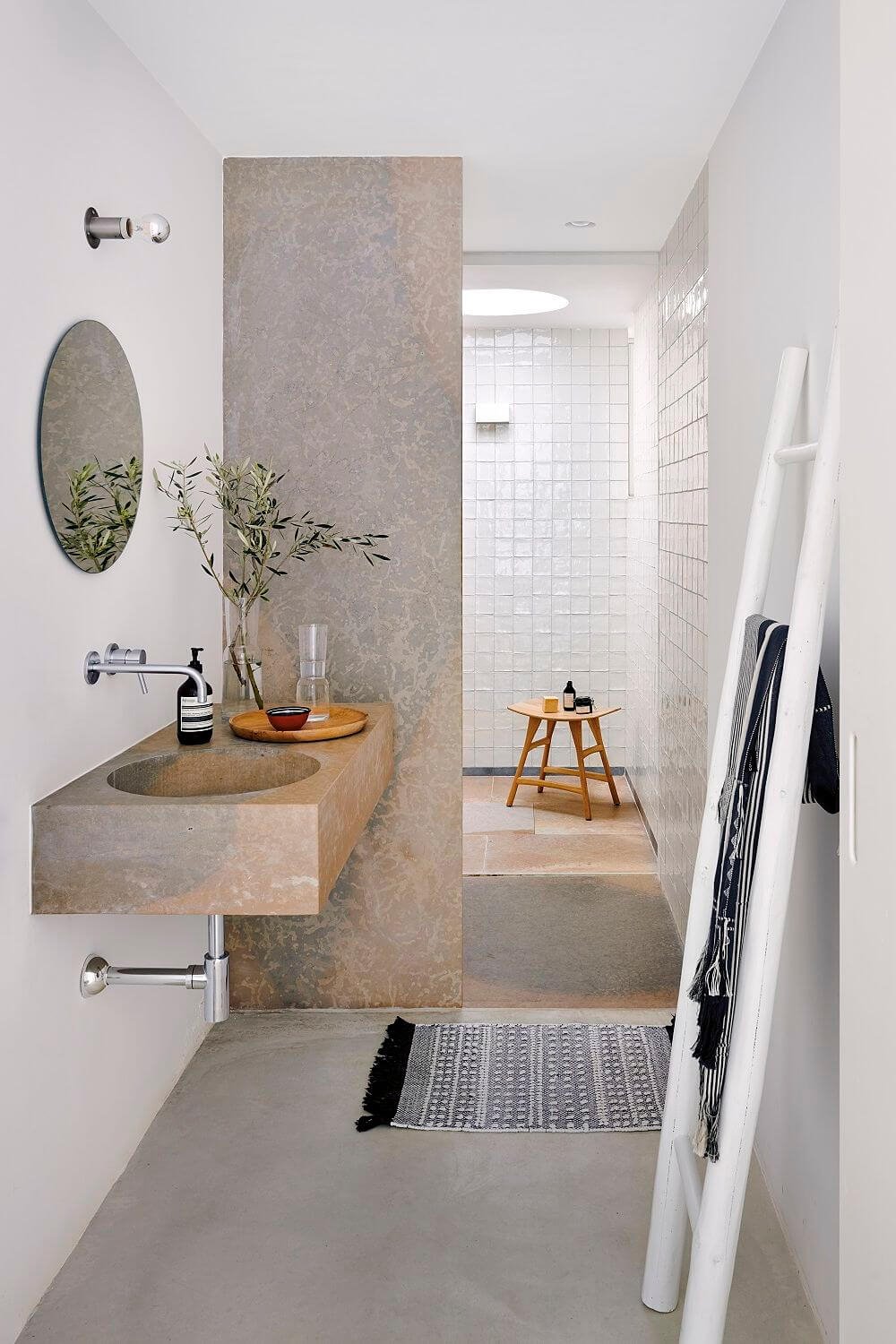 Baño moderno con lavabo suspendido de piedra y ducha al fondo. 