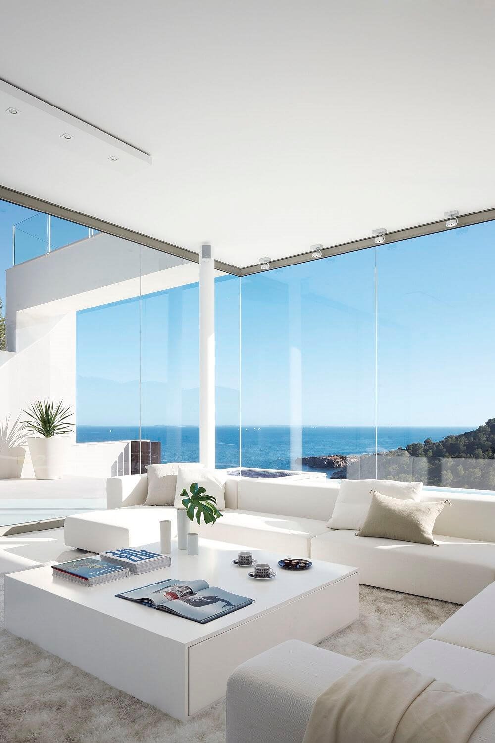 Un precioso y espectacular salón blanco en el que el azul del mar se ha convertido en color secundario siendo el verde de las plantas el utilizado como color de acento.