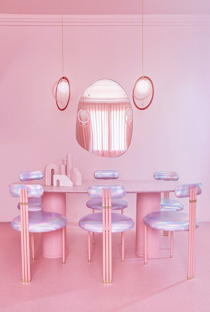 Surrealista comedor en tonos rosa con los asientos de un violeta perlado. 