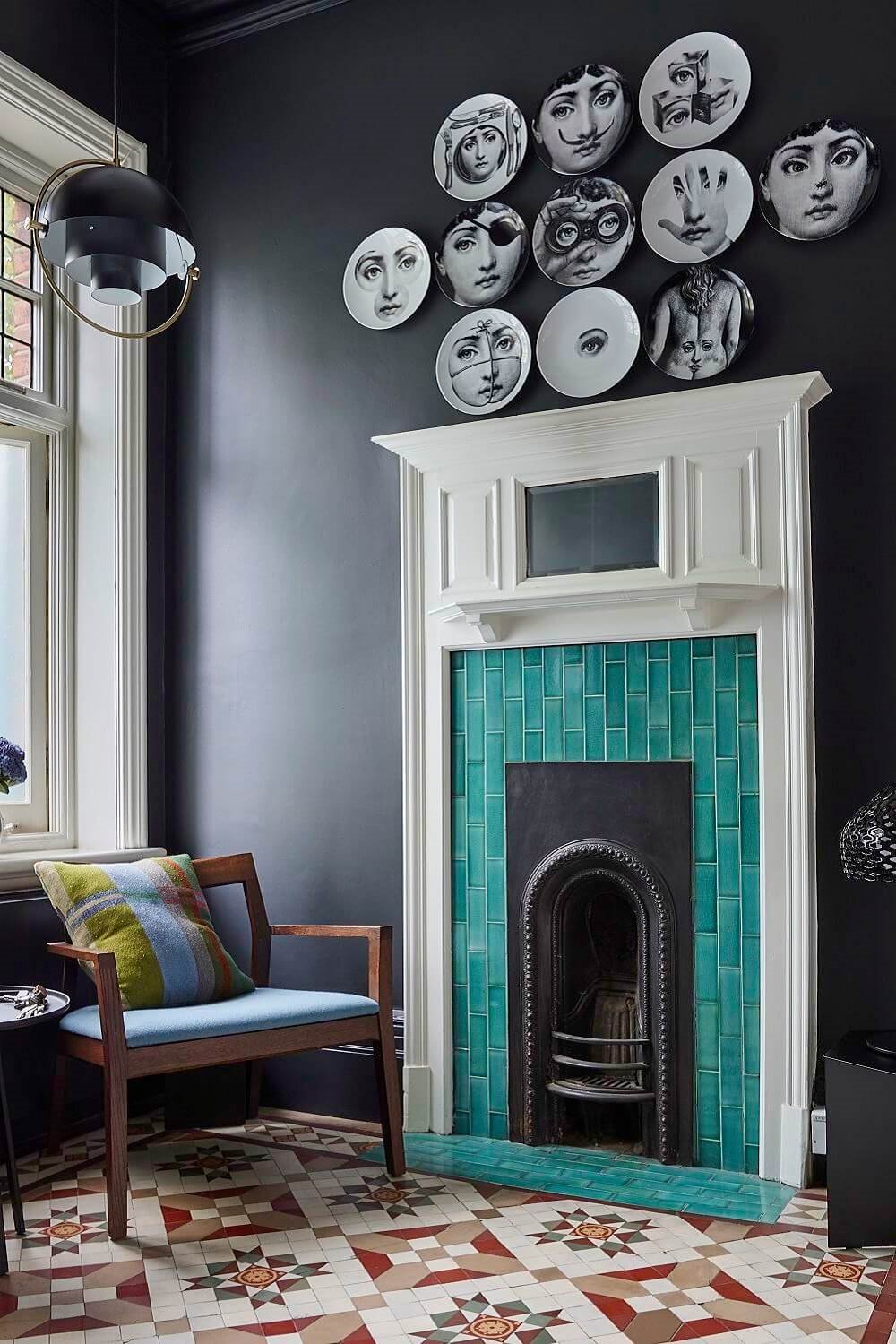 La pared oscura, el contraste con el blanco, la colección de platos y el verde de la chimenea son los trucos decorativos empleados para dar protagonismo a esta pared.
