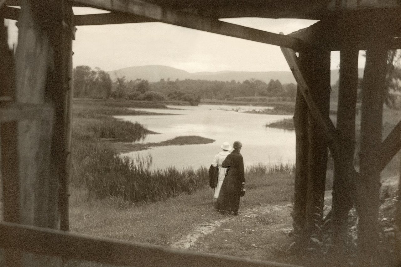 Paisaje con dos mujeres caminando, interesante encuadre a través de una estructura de madera. Margaret Watkins. PhotoEspaña 2021
