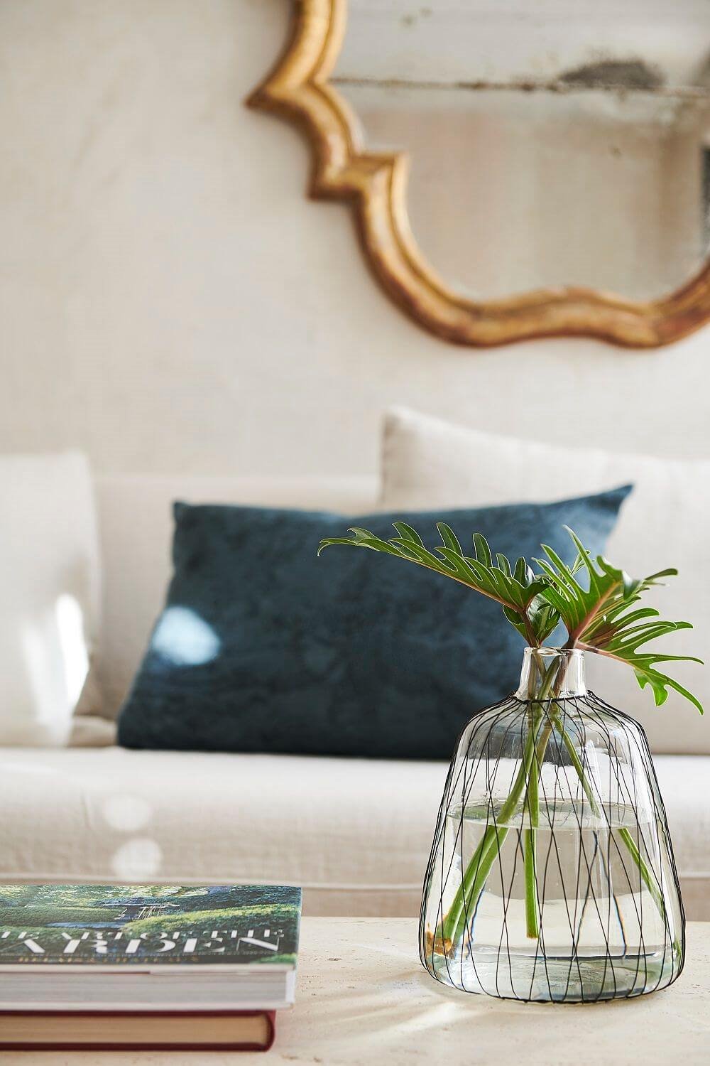 Jarrón de cristal con plantas sofa blanco y espejo dorado