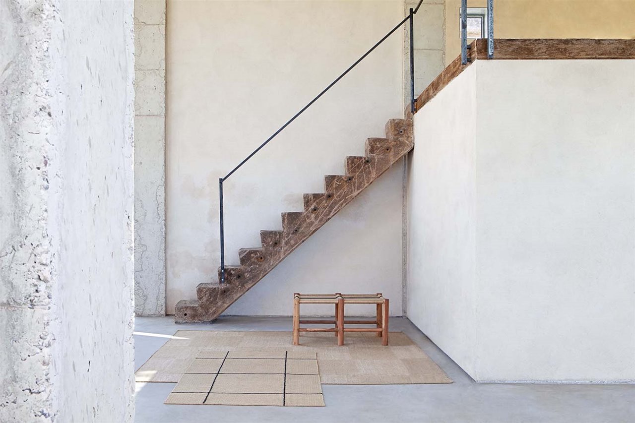 Dos taburetes realizados con madera de acacia y asiento trenzado a mano combinan con los kílims.