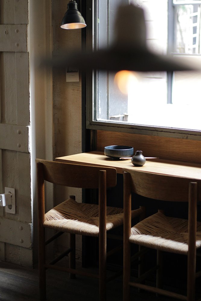 Bajo las ventanas, pequeñas barras en las que comer mientras nuestra mirada pasea por la ciudad, las sillas vintage de estilo nórdico con asiento en cuerda son un diseño de Børge Mogensen