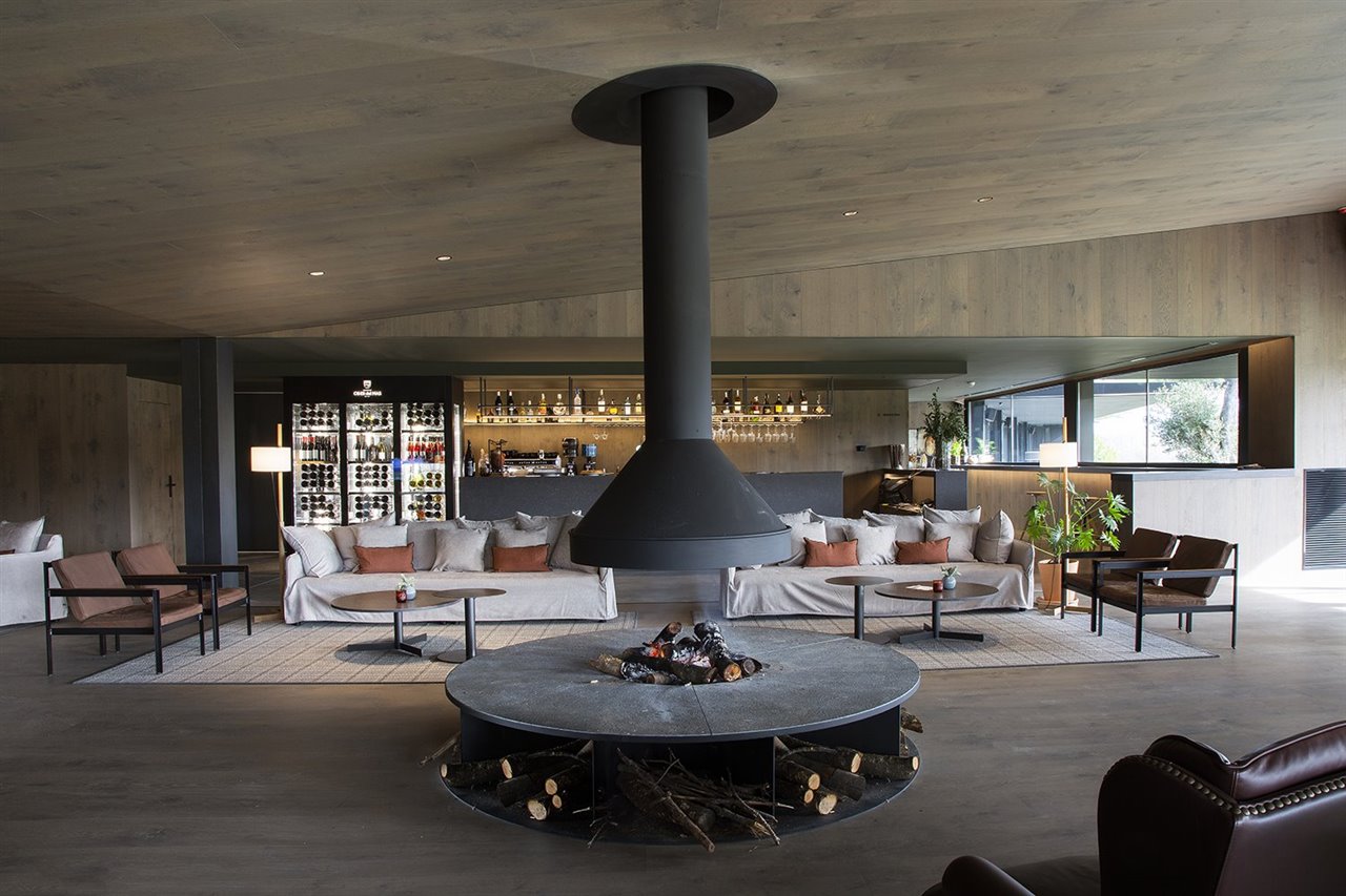 La zona del Wine Bar ofrece una cálida acogida al visitante al más puro estilo de la montaña, alrededor de una gran chimenea circular de leña como punto de reunión.