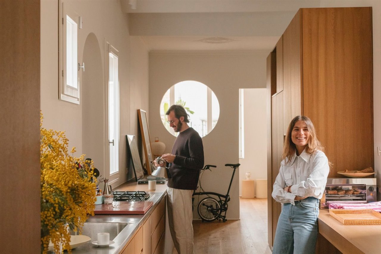 Román y Gabriela en la cocina, que ha evolucionado de espacio meramente dedicado a la circulación a jugar un papel importante en la vida de la casa. Ahora es donde la pareja se encuentra después de un día de trabajo o donde sus amigos se reúnen mientras alguien está cocinando. La cocina ha reorganizado completamente la lógica interna del espacio y cómo interactúan con él.
