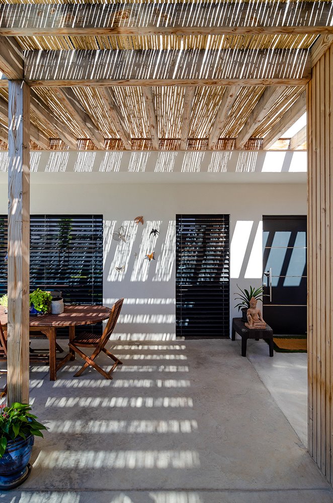 La pérgola, cubierta en el porche con fibra vegetal, crea un espacio intersticial en sombra a través del cual se accede a la casa.
