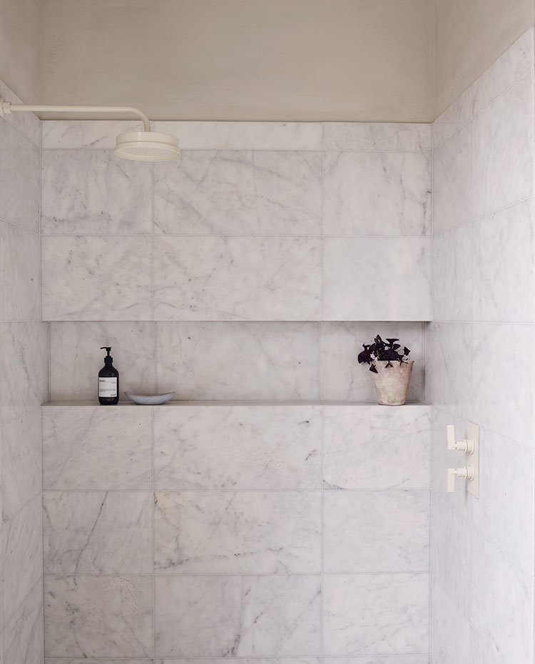 Zona ducha con hornacina de obra revestida de marmol, griferi´a acabada en blanco