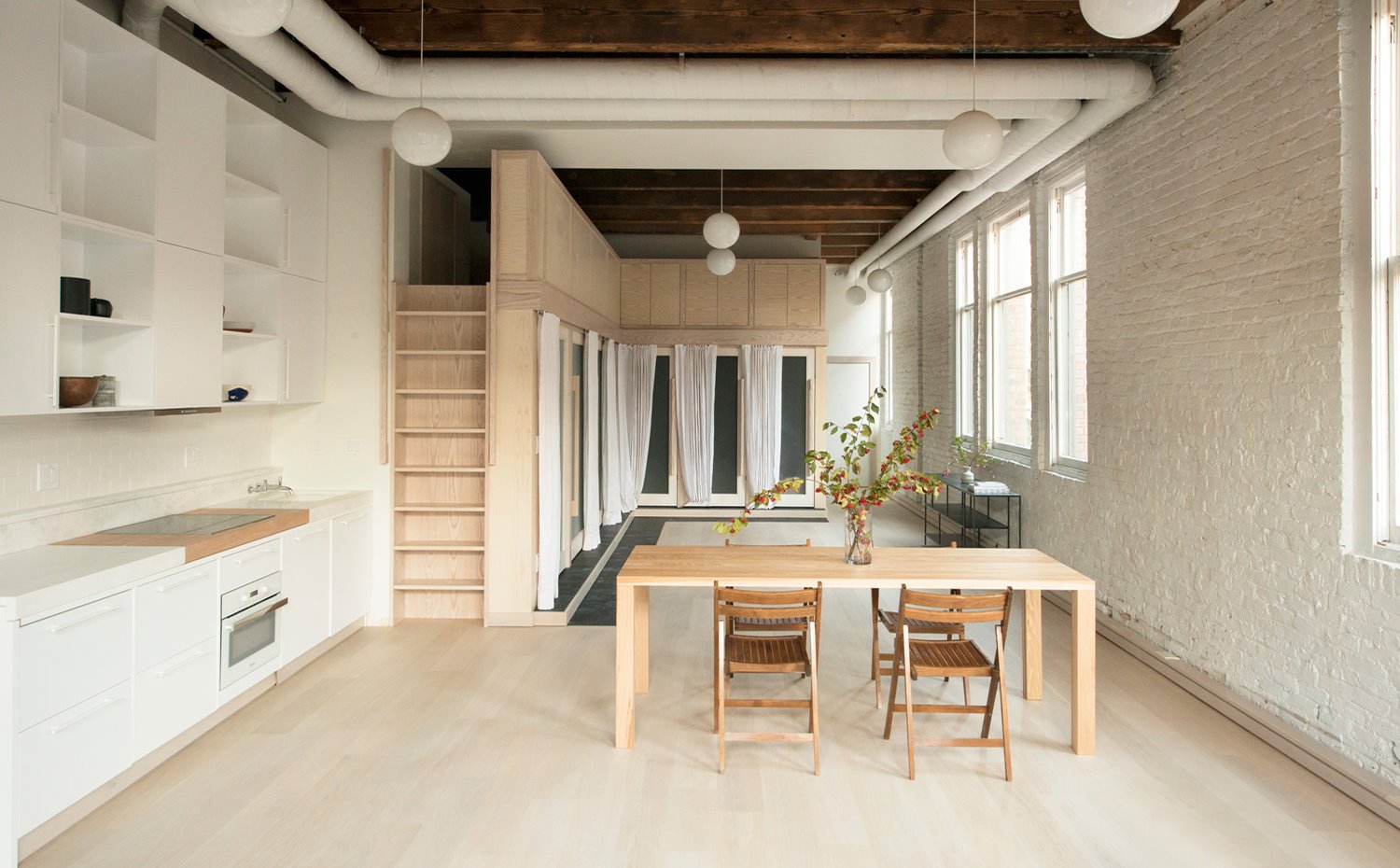 Mesa comedor, sillas plegables madera, escalera vertical, cocina blanca, conductos de aire en blanco, loft industrial
