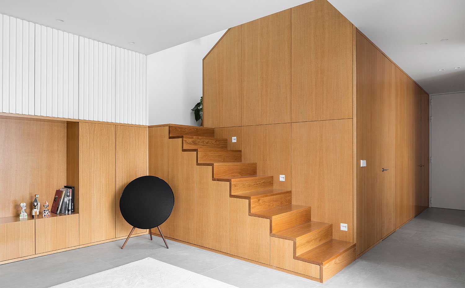Salón con altavoz de formas circulares, mueble de almacenaje revestido de madera natural, a juego con las escaleras