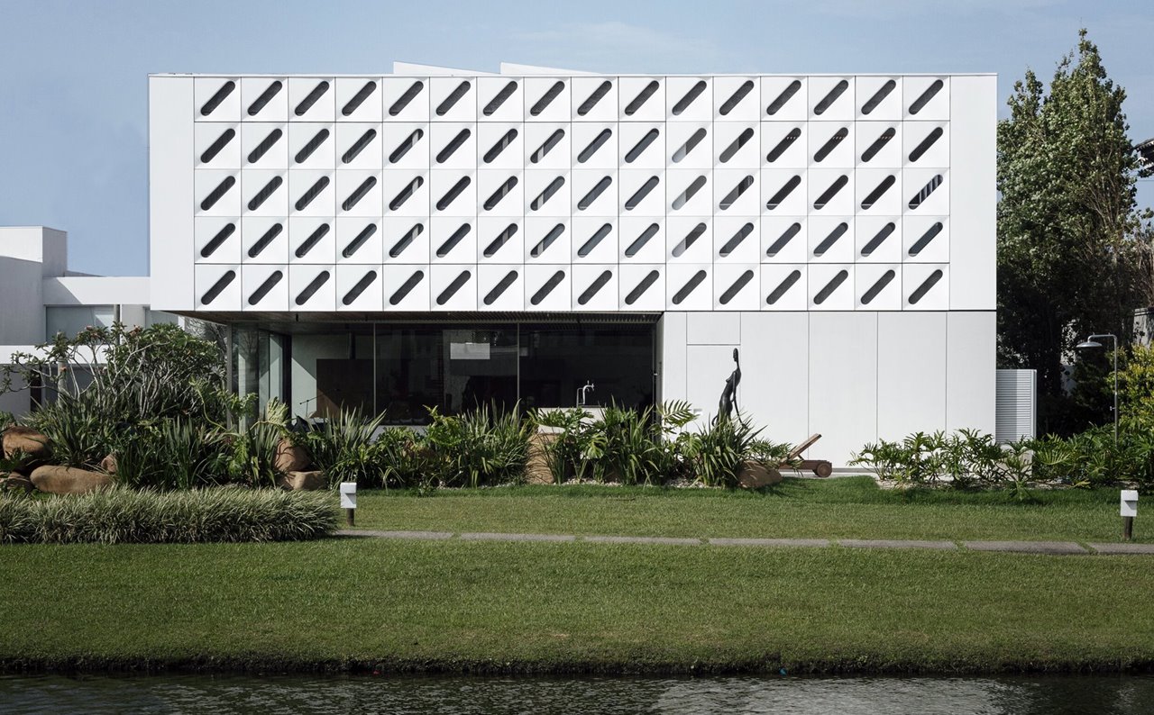 Un panel perforado blanco envuelve la fachada de esta casa de playa en Brasil.