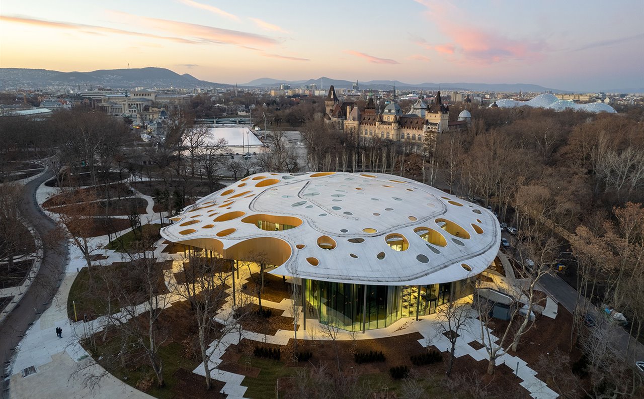 El edificio se ubica en el City Park, el parque central de Budapest, y se caracteriza por su cubierta ondulada y perforada.
