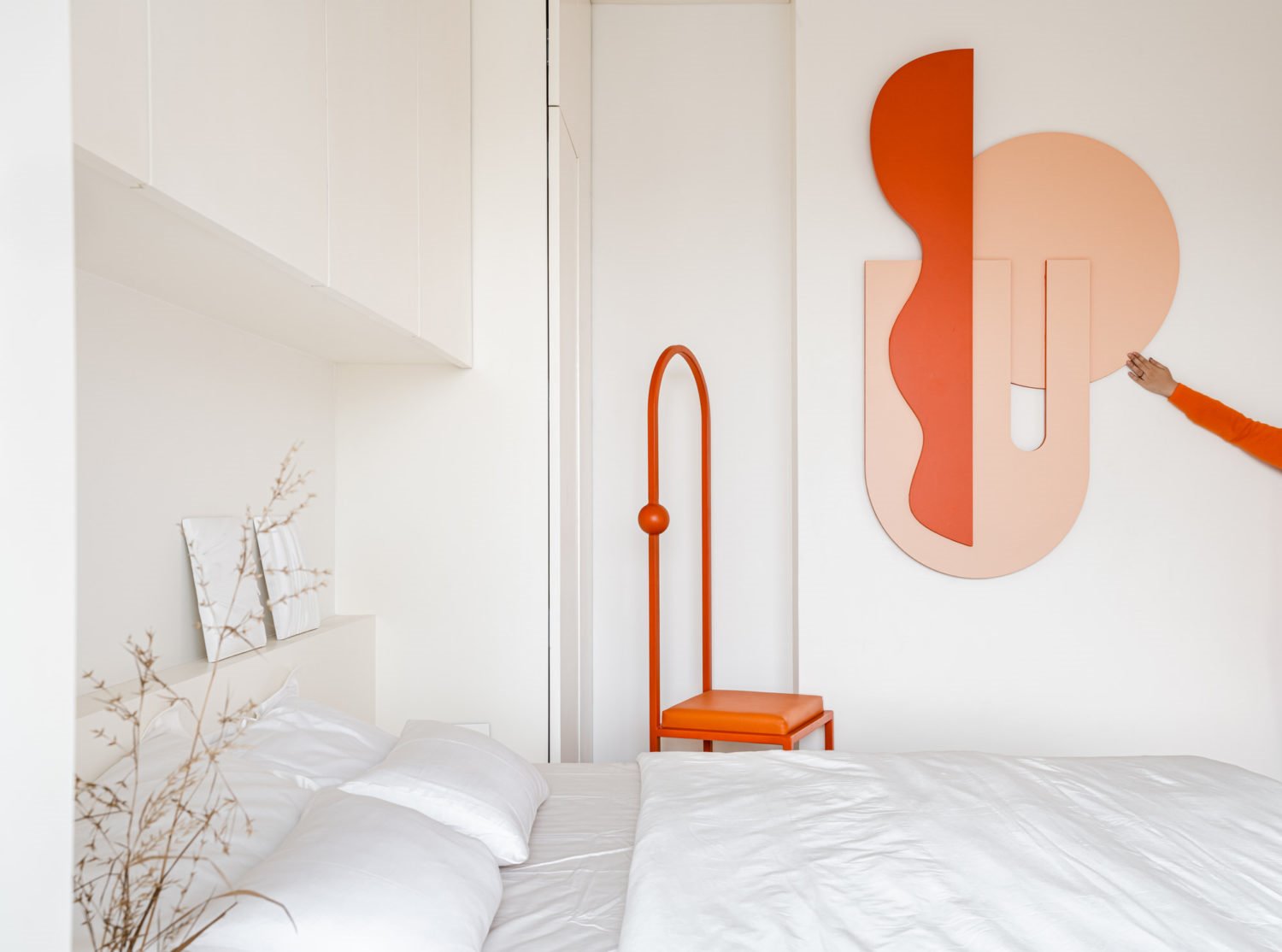 Dormitorio blanco con silla y adornos geométricos en rojo y salmón.