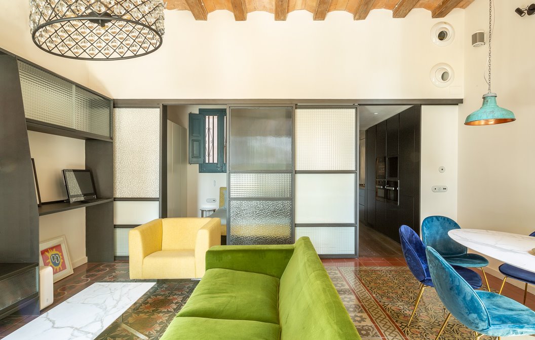 Salón con paredes beige, sofá verde, butaca amarilla y sillas de comedor azules. 