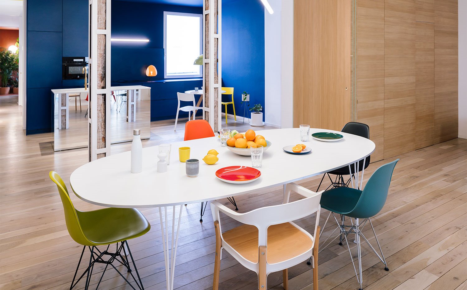 Mesa de comedor en blanco, con sillas en diferentes diseños y colores, carpintería en madera natural, pared del fondo en azul