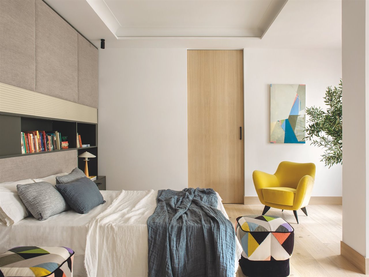 Dormitorio de un piso en Madrid con butaca de color amarillo y taburete de colores