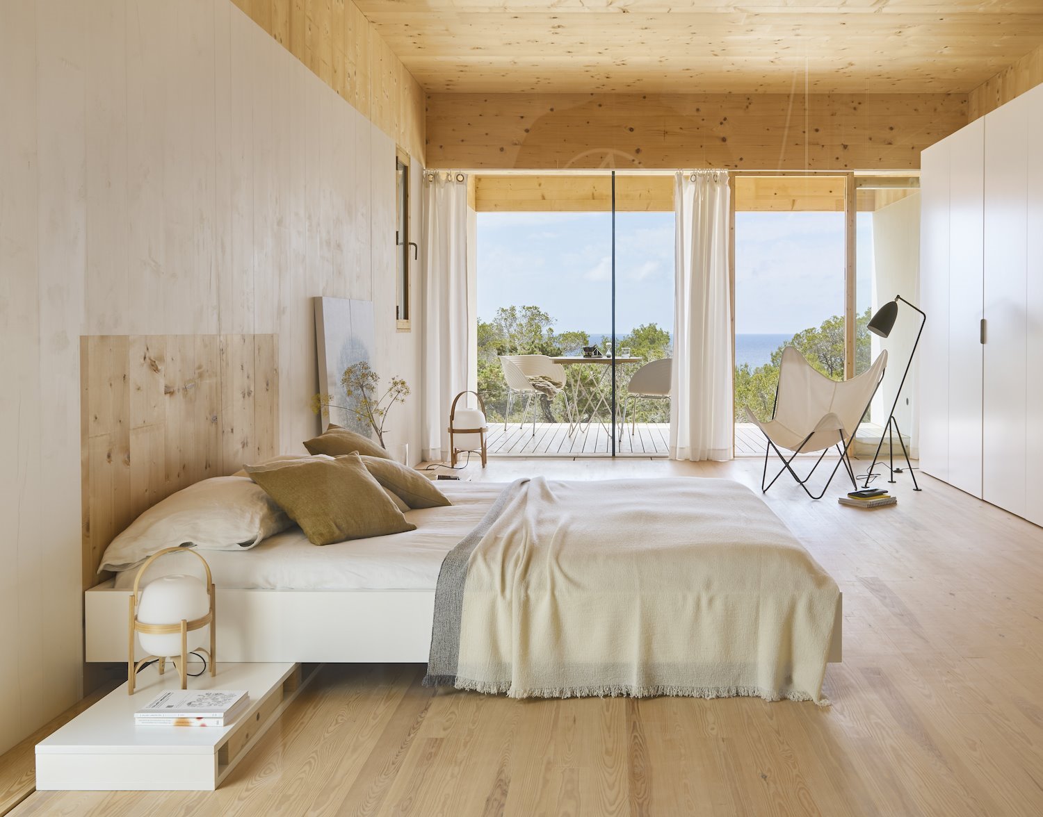 Dormitorio con revestimientos de madera y una cama con ropa blanca y color crema.