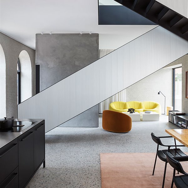 Vista de escalera como eje central de espacio, con la cocina y comedor en un lado y zona de estar al fondo