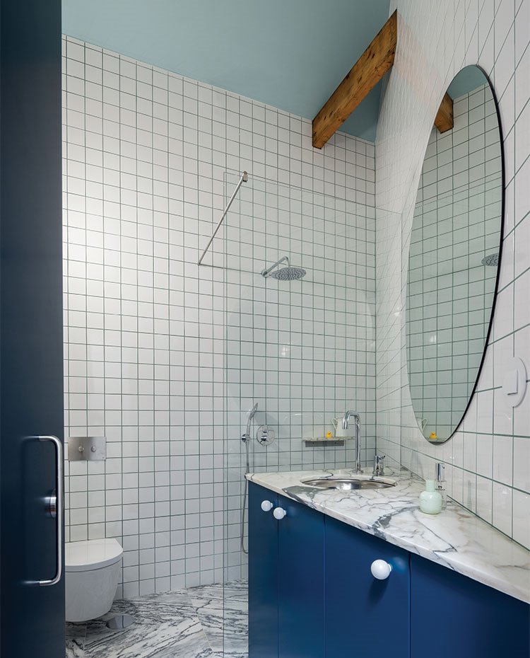 Cuarto de baño con suelo y encimera de mármol, mueble bajolavabo en azul, espejo ovalado
