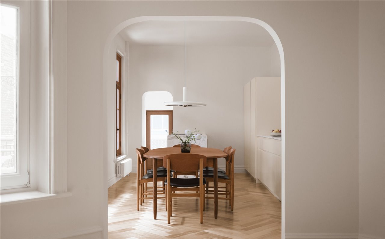 La mesa de comedor conversa con el diseño de cocina sencillo que sigue la forma rectangular del espacio. La adición de una abertura arqueada entre la sala de estar y la cocina acentúa las vistas entre zonas, al mismo tiempo que mejora el flujo.