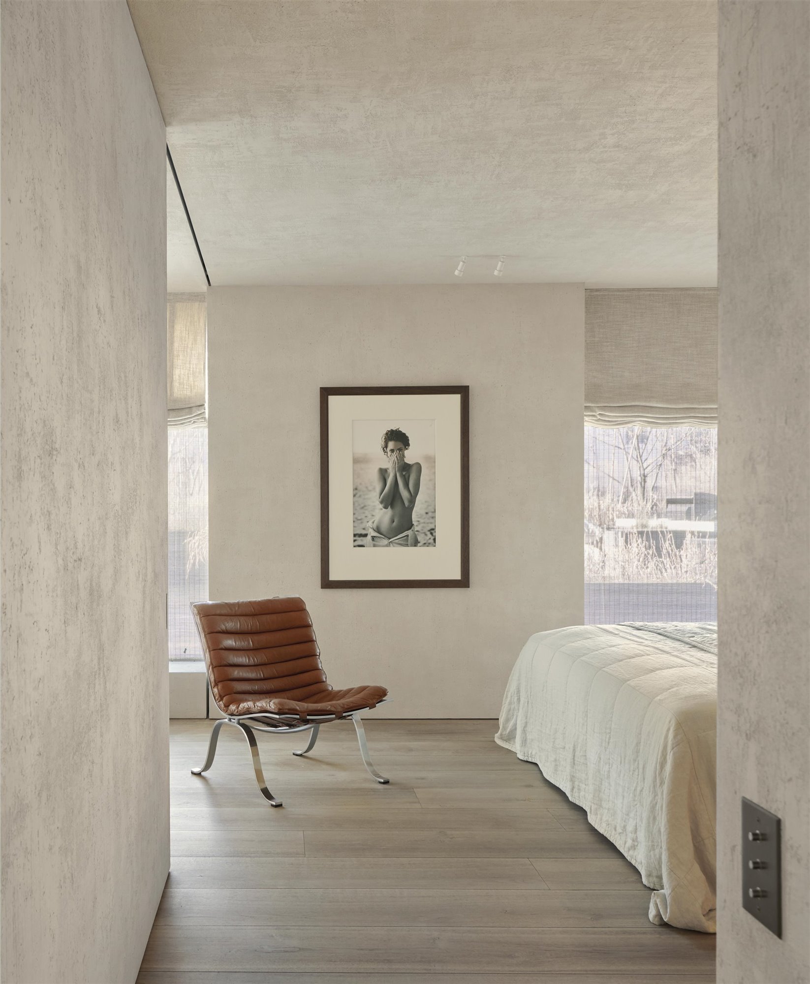 dormitorio cama blanca, butaca de piel y fotografía en la pared de peter lindbergh