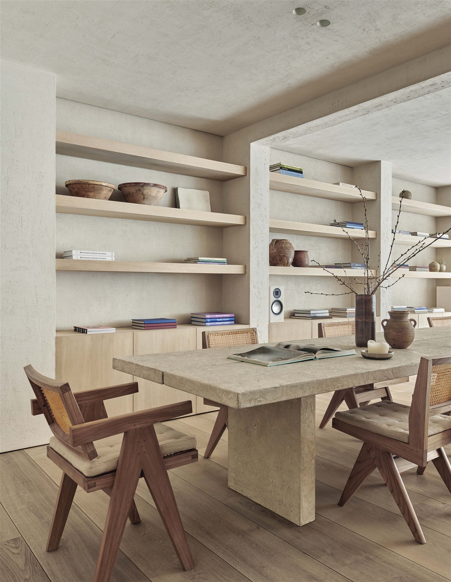 Mesa comedor de cemento con silla de madera y mimbre, jarrón y estantería minimalista estilo japonés.