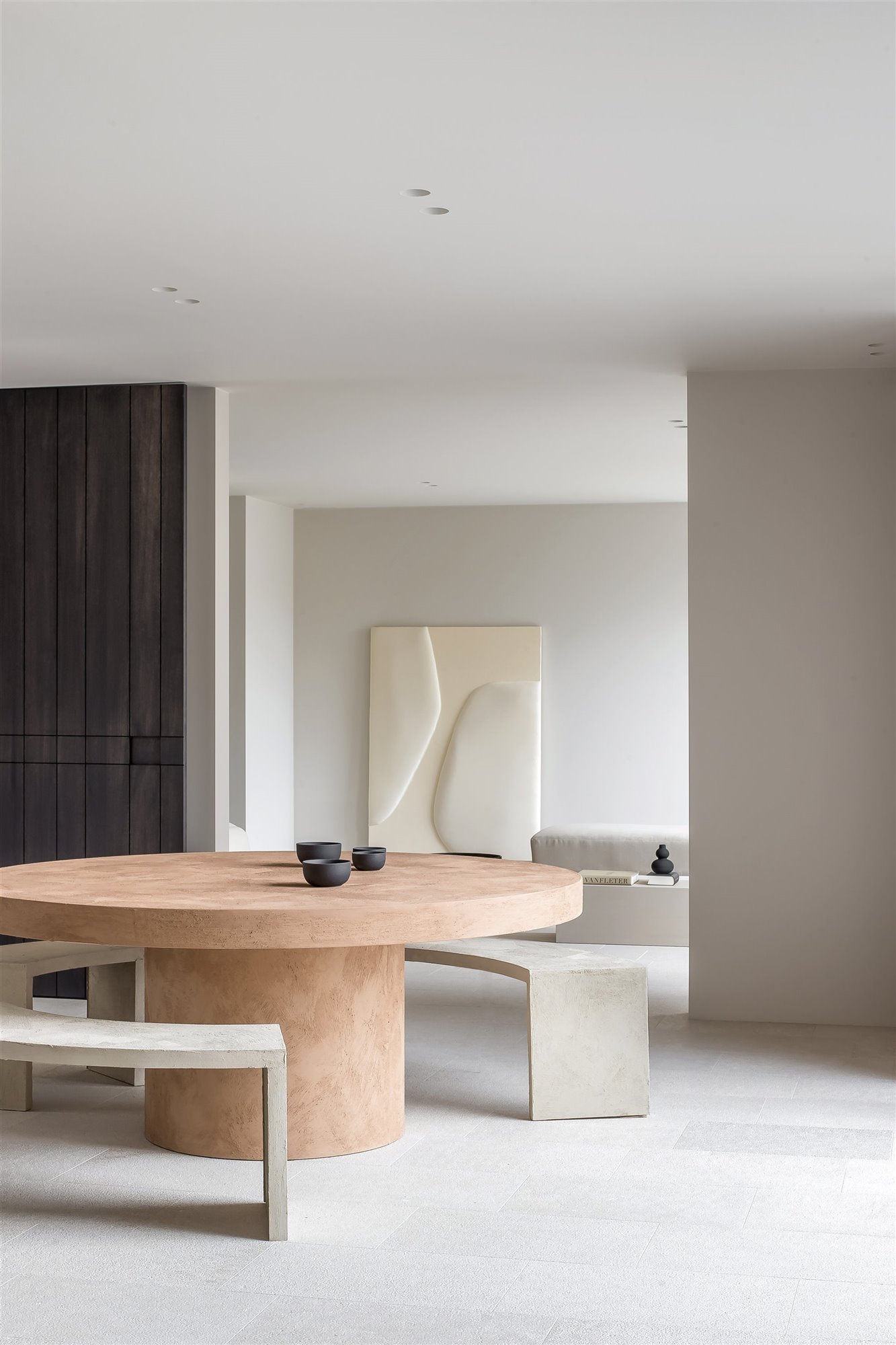 mesa comedor redonda con bancos y cuencos negros en un salón minimalista blanco