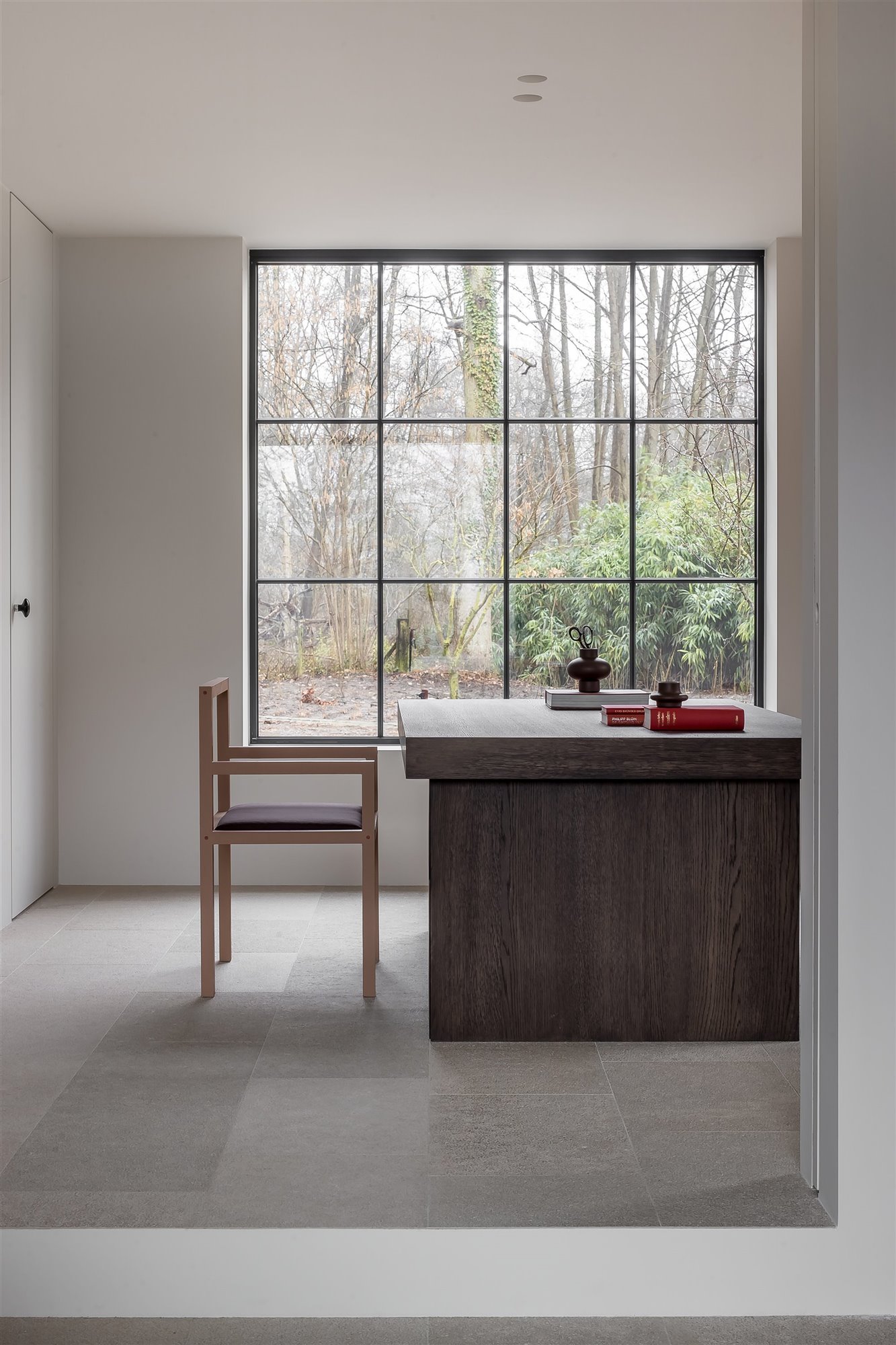 mesa de escritorio de madera oscura con ventana grande, libros rojos y cuencos 
