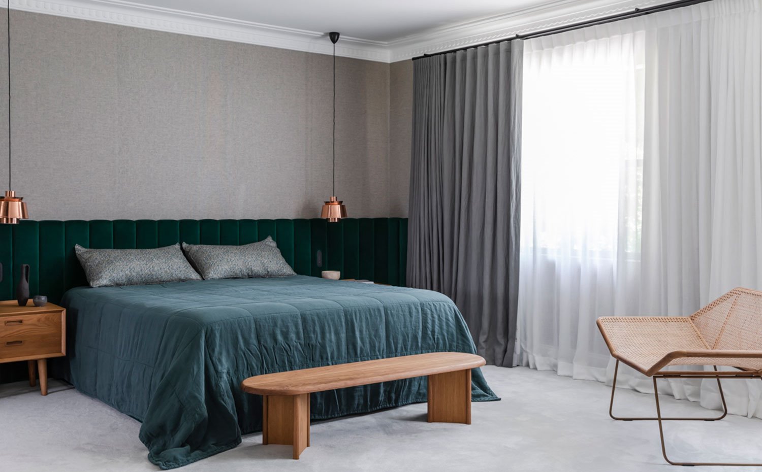 Dormitorio con bancada a los pies de la cama, butaca de fibra, mesita de noche de madera y luminarias suspendidas con pantalla de latón