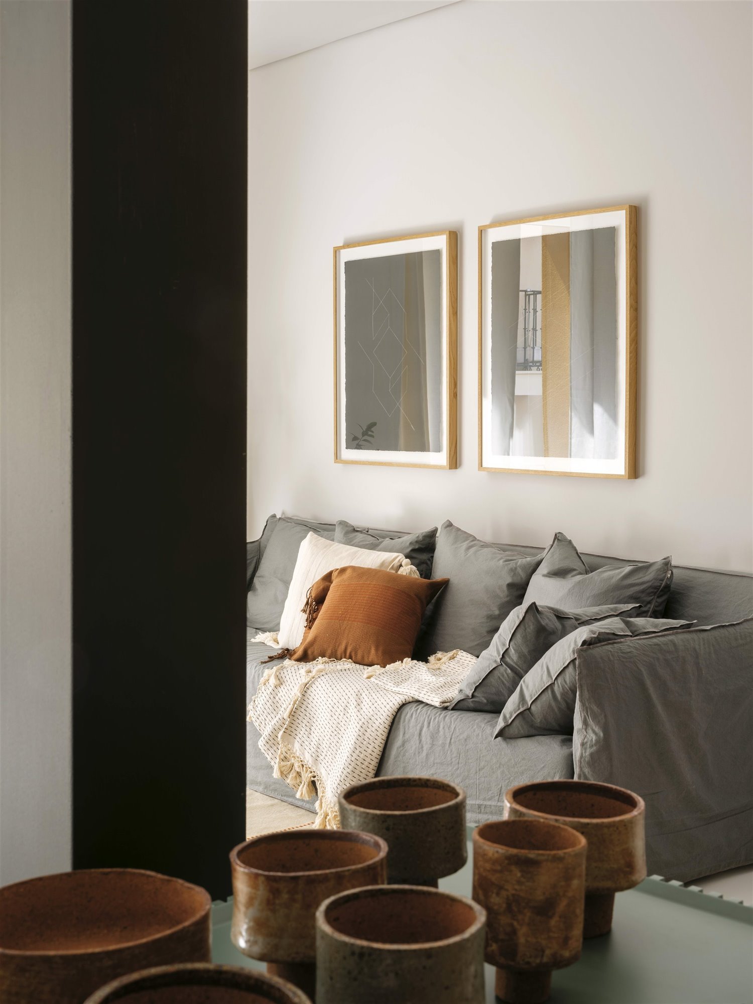 Salón con sofá gris y cojin marrón, cuencos de cerámica.