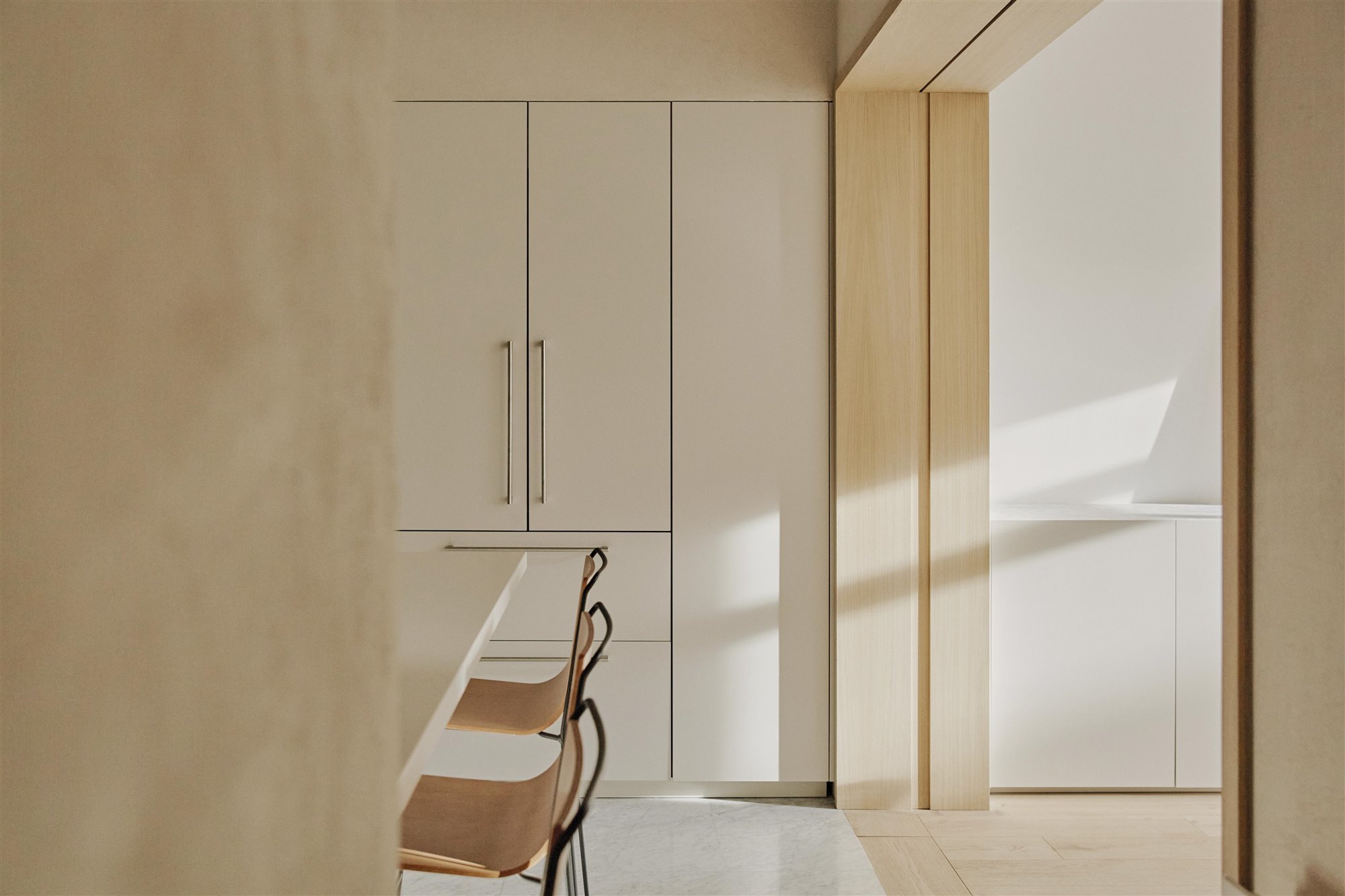 cocina minimalista beige con taburetes de madera, isla blanca y mueble