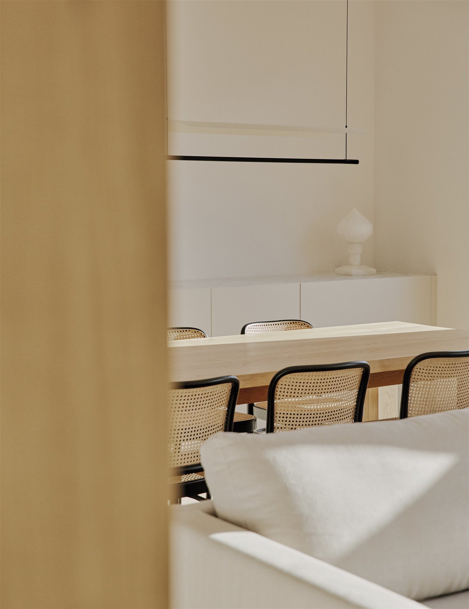 comedor minimalista beige con mesa de madera y sillas, mueble blanco, sofá y lámpara