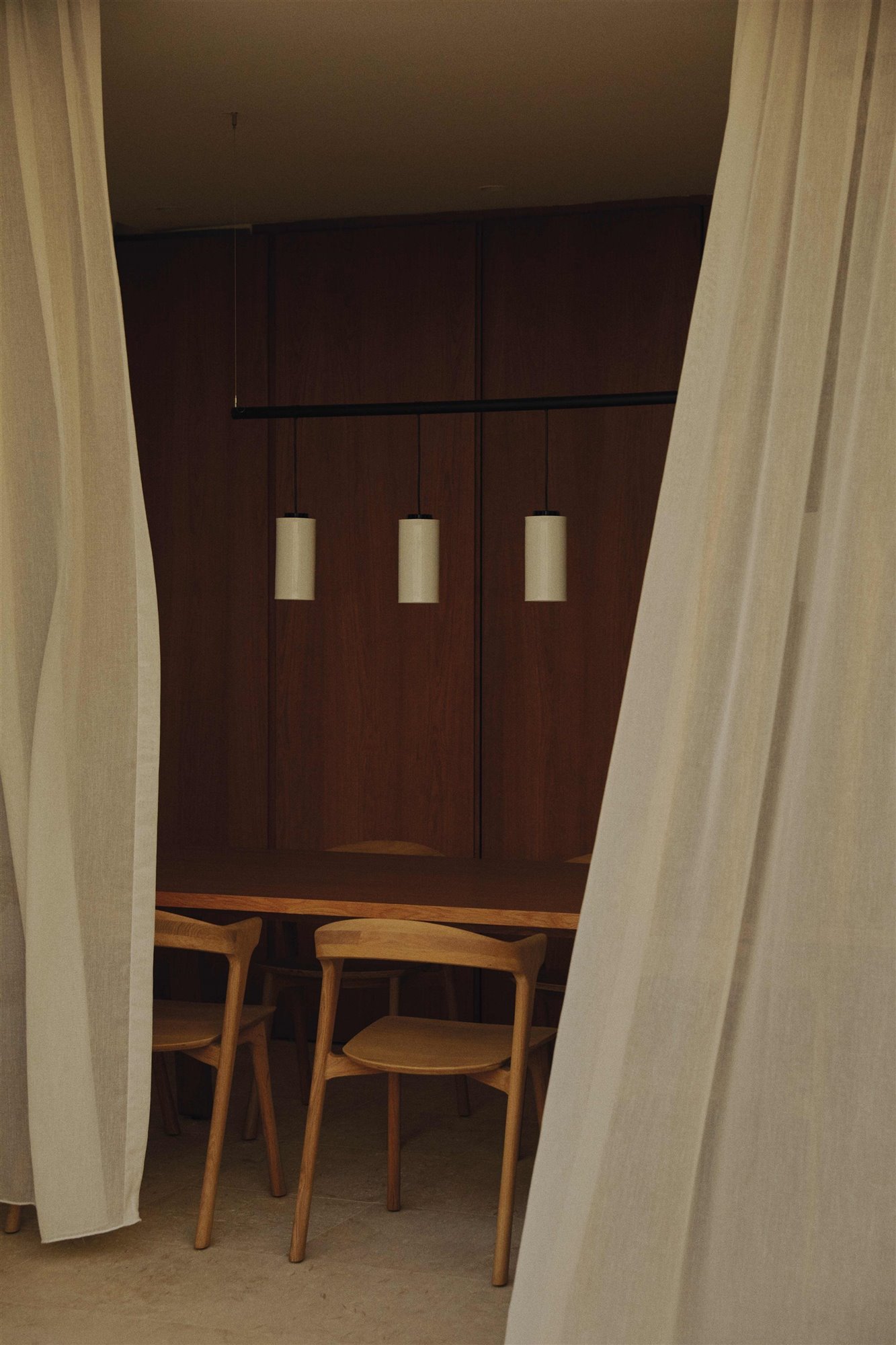 comedor oscuro con cortinas blancas, lámpara de techo, mesa y sillas de madera