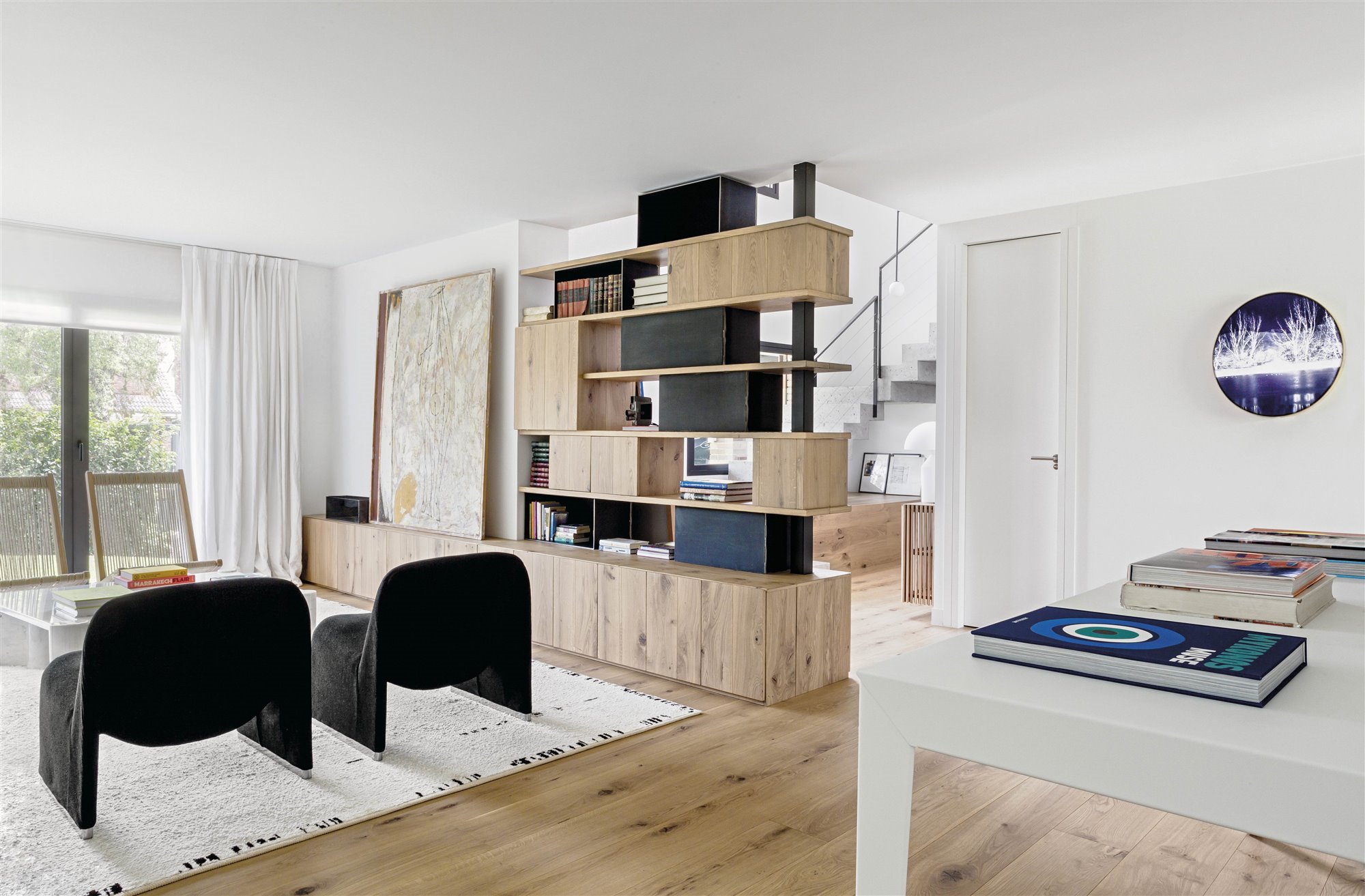 salón contemporáneo con butaca negra, alfombra blanca, estantería de madera y libros