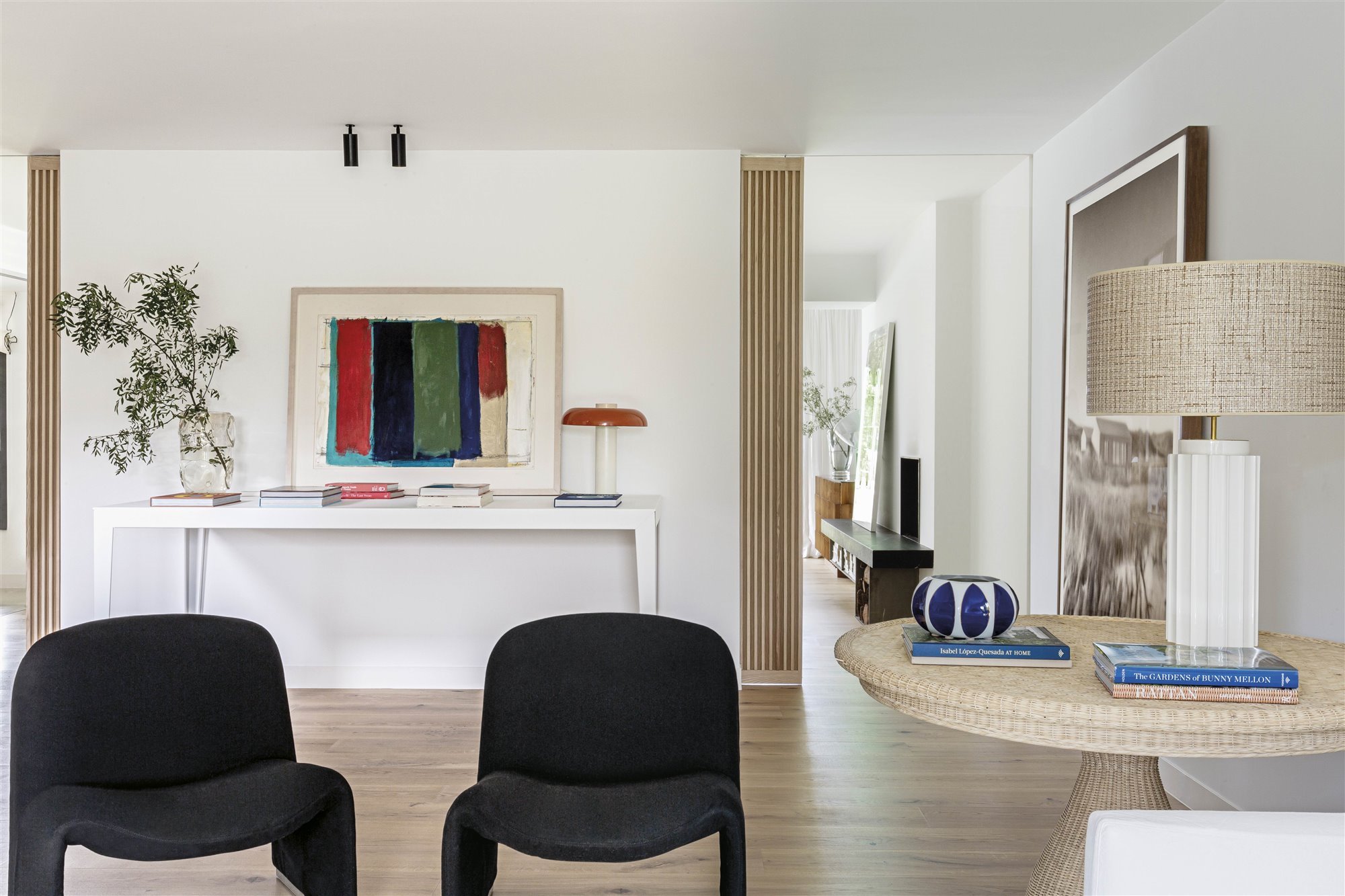 salón contemporáneo con butaca negra, mesa redonda de mimbre, lámpara, cuadro y libros