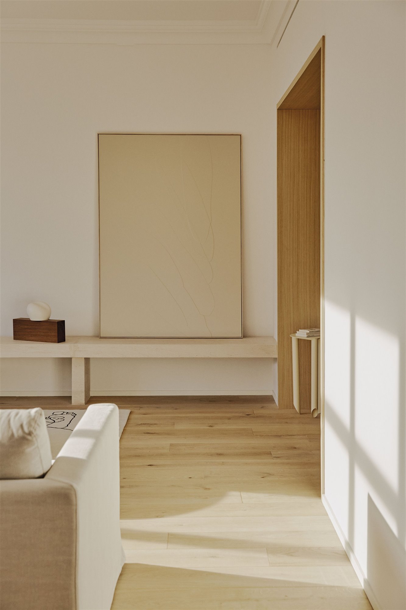 salón minimalista blanco con sofá, alfombra, cuadro y escultura de madera