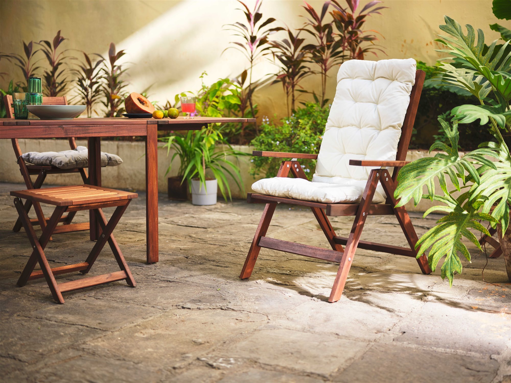 tumbona de madera de exterior con cojin blanco y mesa en un patio con plantas