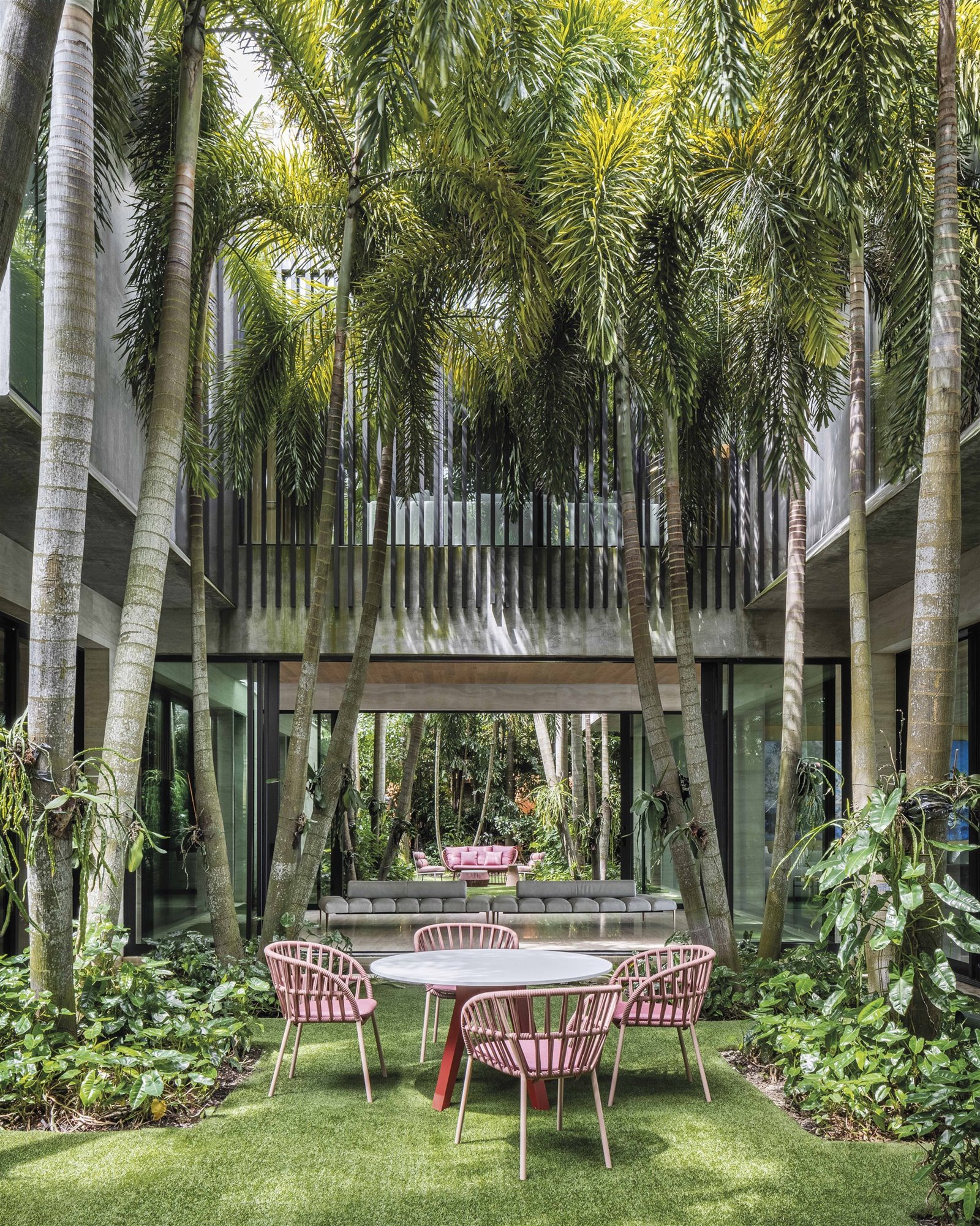 casa con jardín y palmeras mesa redonda y sillas rojas