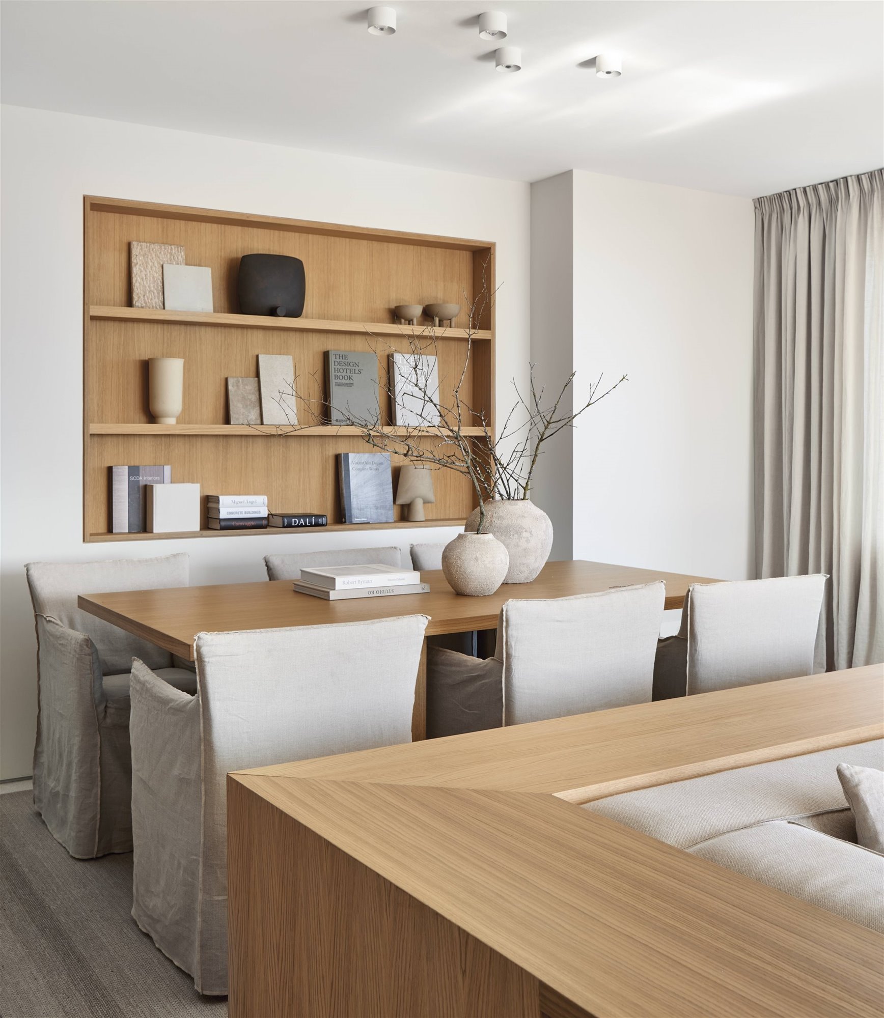 comedor con mesa de madera, sillas beige, estantería, jarrones