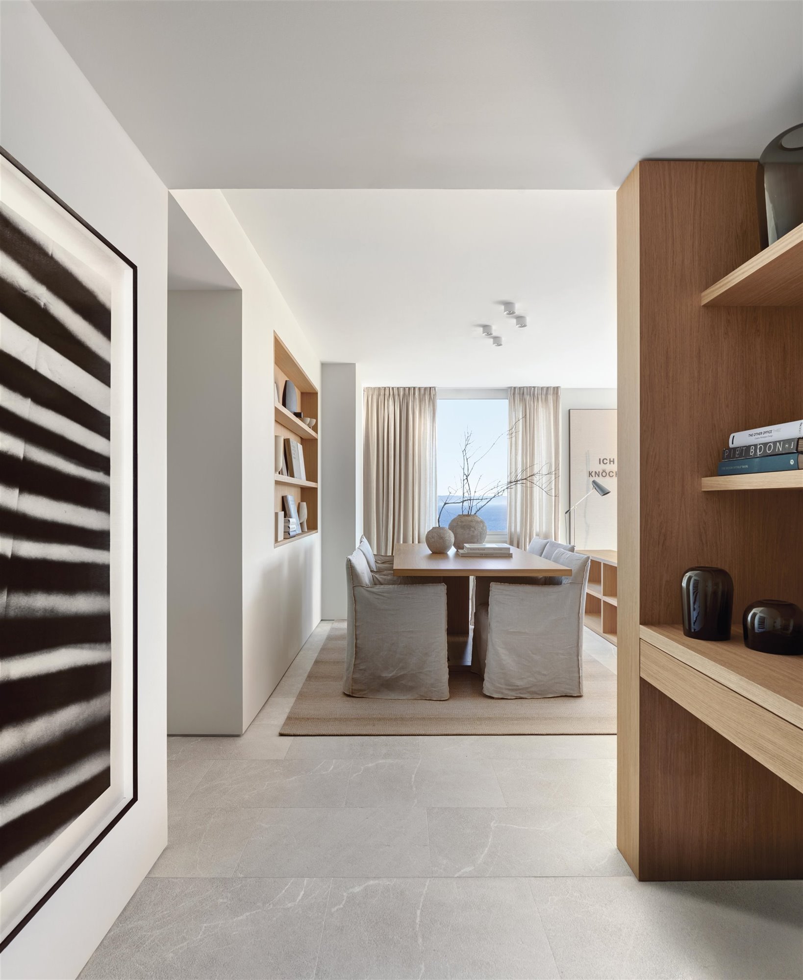 pasillo con comedor al fondo, mesa de madera y butacas con tela beige